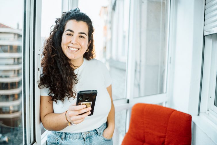 Young freelancer student woman checking his phone while working at home an receiving new deals and preparing his day. Concept of remote work from home, getting ready, new job smiling to camera